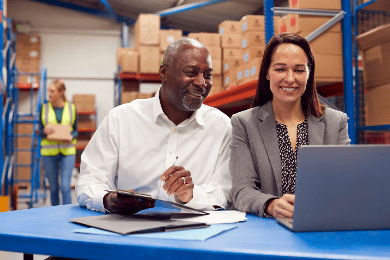 Team leaders using laptop in warehouse with staff behind