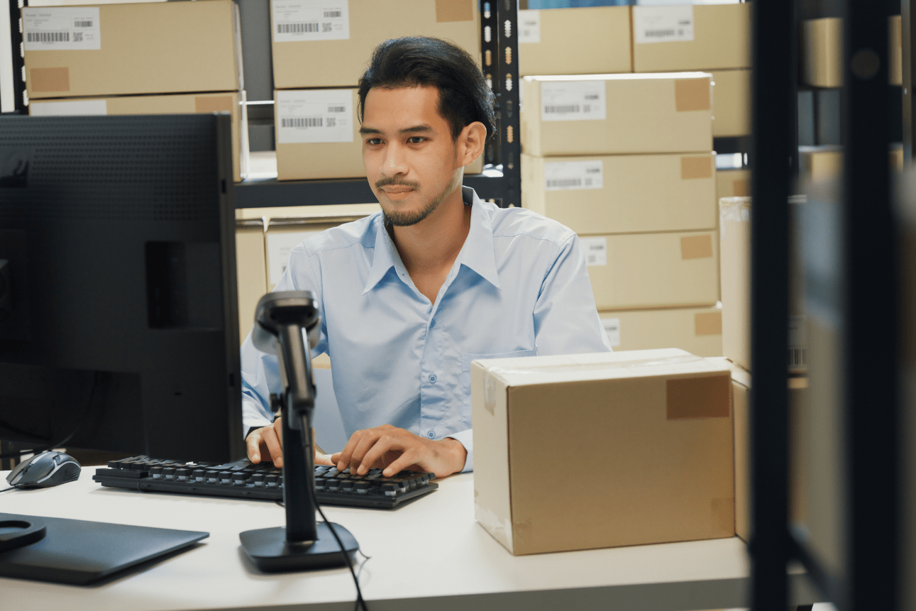 Asian office worker using computer and barcode scanner at logistics workstation